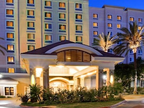Entrada de un hotel con vestíbulo cubierto, varios pisos y fachada bien iluminada.