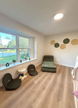 Una habitación con un ventanal grande, un sofá verde, una mesita y una silla.