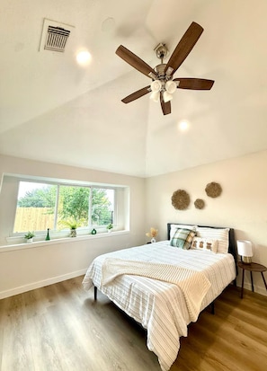 A bedroom with a ceiling fan, a large window, a bed with a striped bedspread, and decorative wall art. - The Shenandoah Sanctuary: A Fully Furnished Modern Retreat (Richmond)