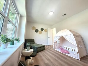 Una habitación con una cama, una silla verde, una mesita pequeña y una estructura parecida a una tienda de campaña.
