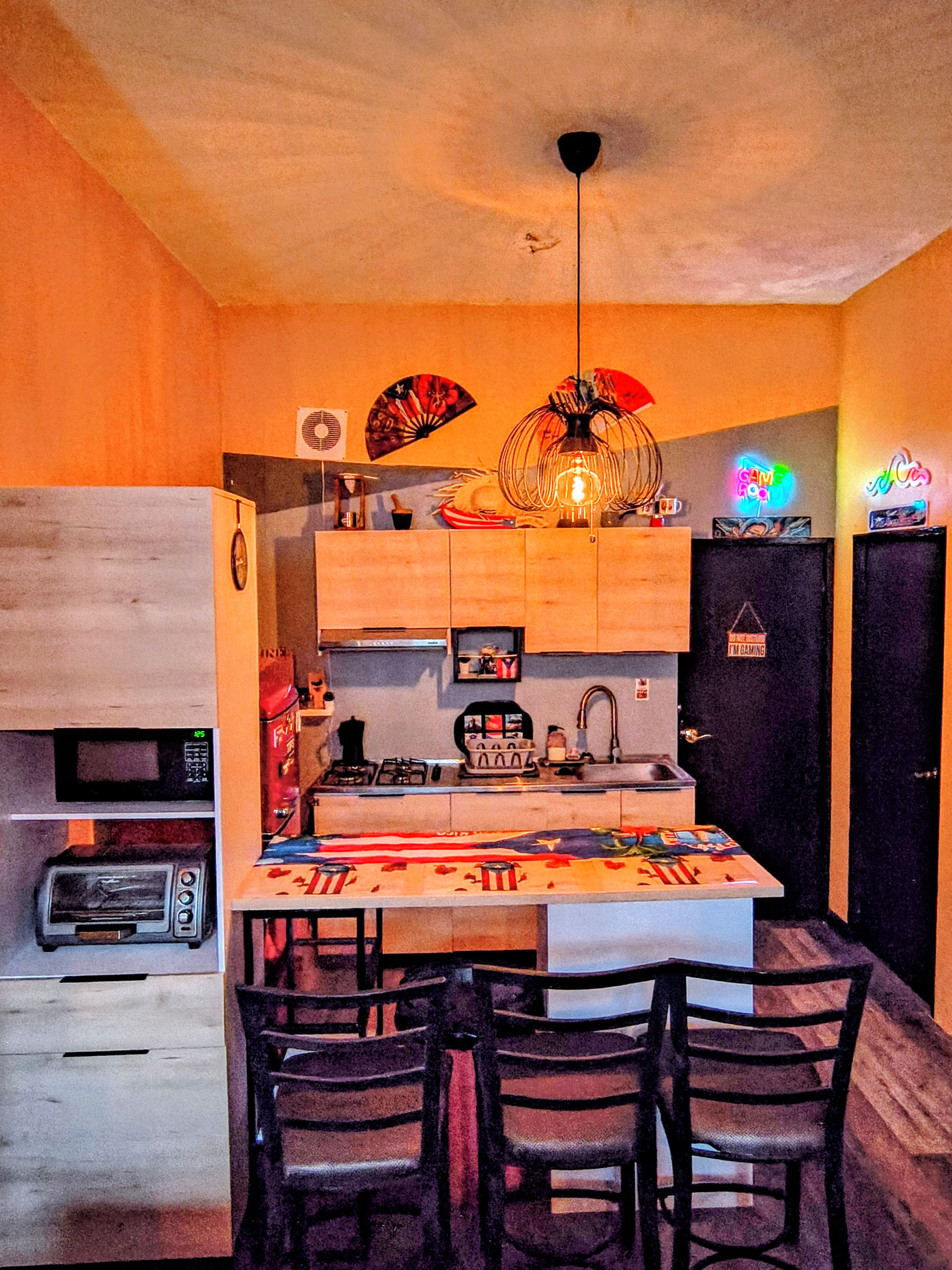 Une cuisine compacte dotée d’un îlot central, d’un four à micro-ondes, d’une cuisinière à gaz et d’un coin repas avec des chaises.