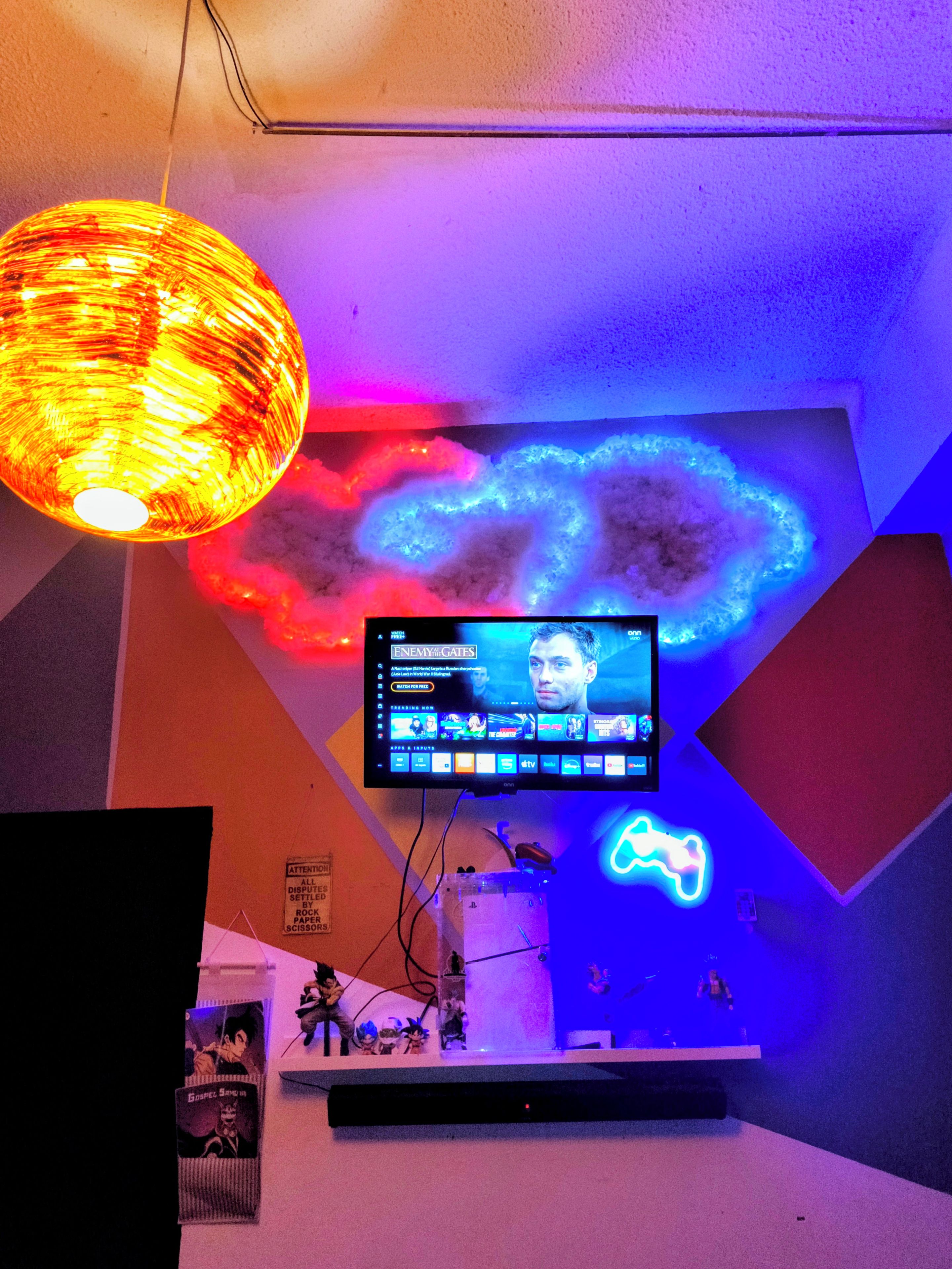 A room with a television mounted on the wall, a neon light, and a shelf with various items.