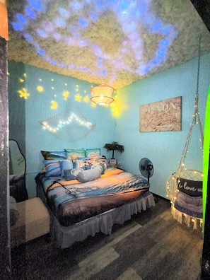 Una camera da letto con un letto, una sedia a dondolo, un ventilatore a parete e una lampada a soffitto.