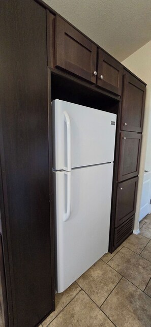 Eine Küche mit einem weißen Kühlschrank, dunklen Holzschränken und einem gefliesten Boden.