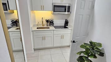 Uma cozinha compacta com armários brancos, micro-ondas e cafeteira.