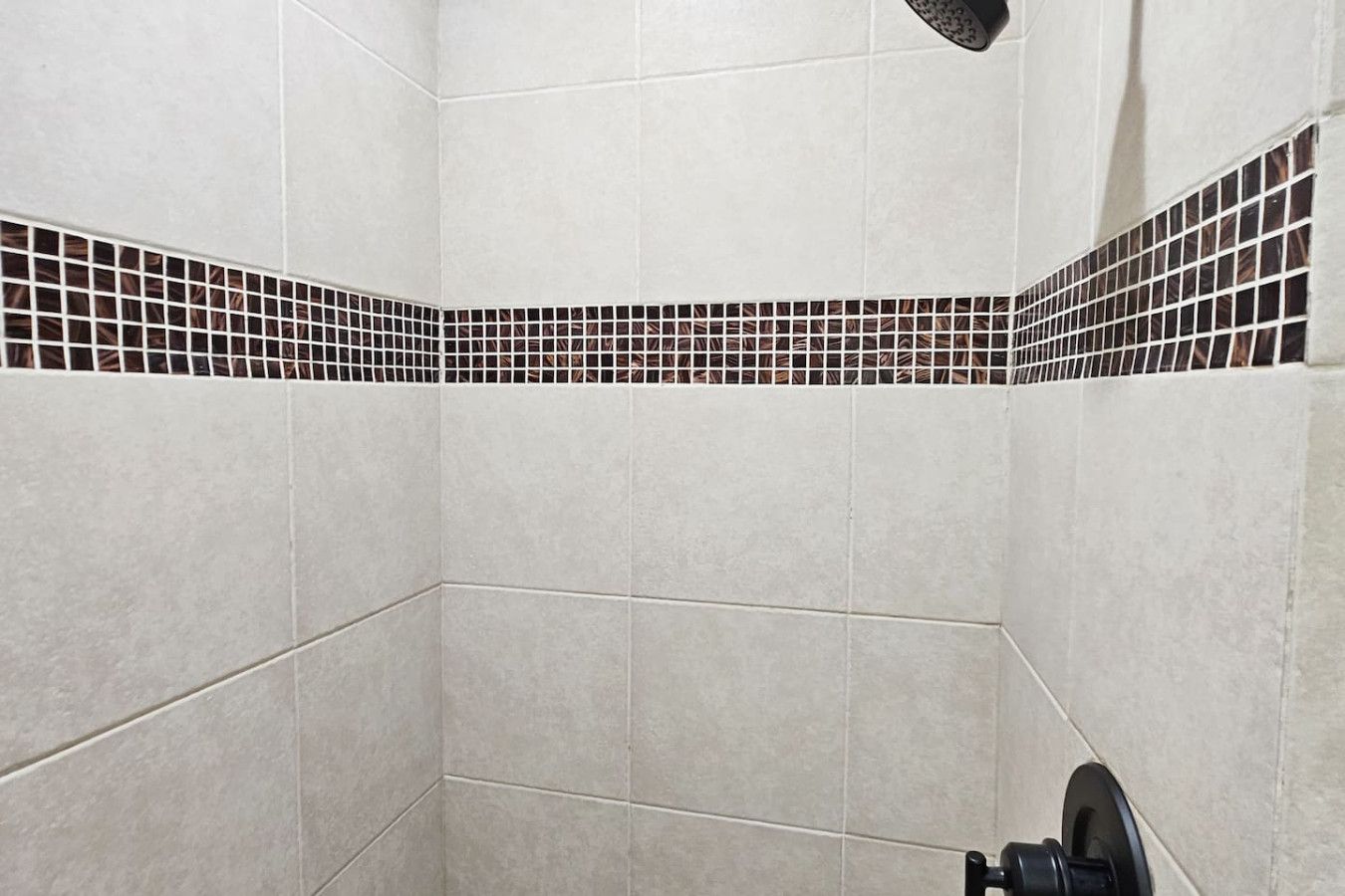 Canto de um banheiro com azulejos brancos e borda de mosaico preto e branco.