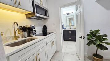 A modern kitchen with white cabinetry, a stainless steel microwave, a coffee maker, and a sink.
