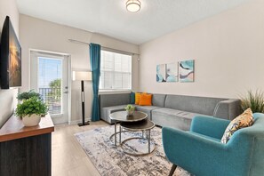 A modern living room with a sofa, a coffee table, a blue armchair, and a flat-screen TV mounted on the wall. - Vista Cay 3BR Condo Pools Near Universal (Orlando)