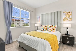 A bedroom with a bed, two bedside tables, a window with curtains, and artwork on the walls. - Vista Cay 3BR Condo Pools Near Universal (Orlando)