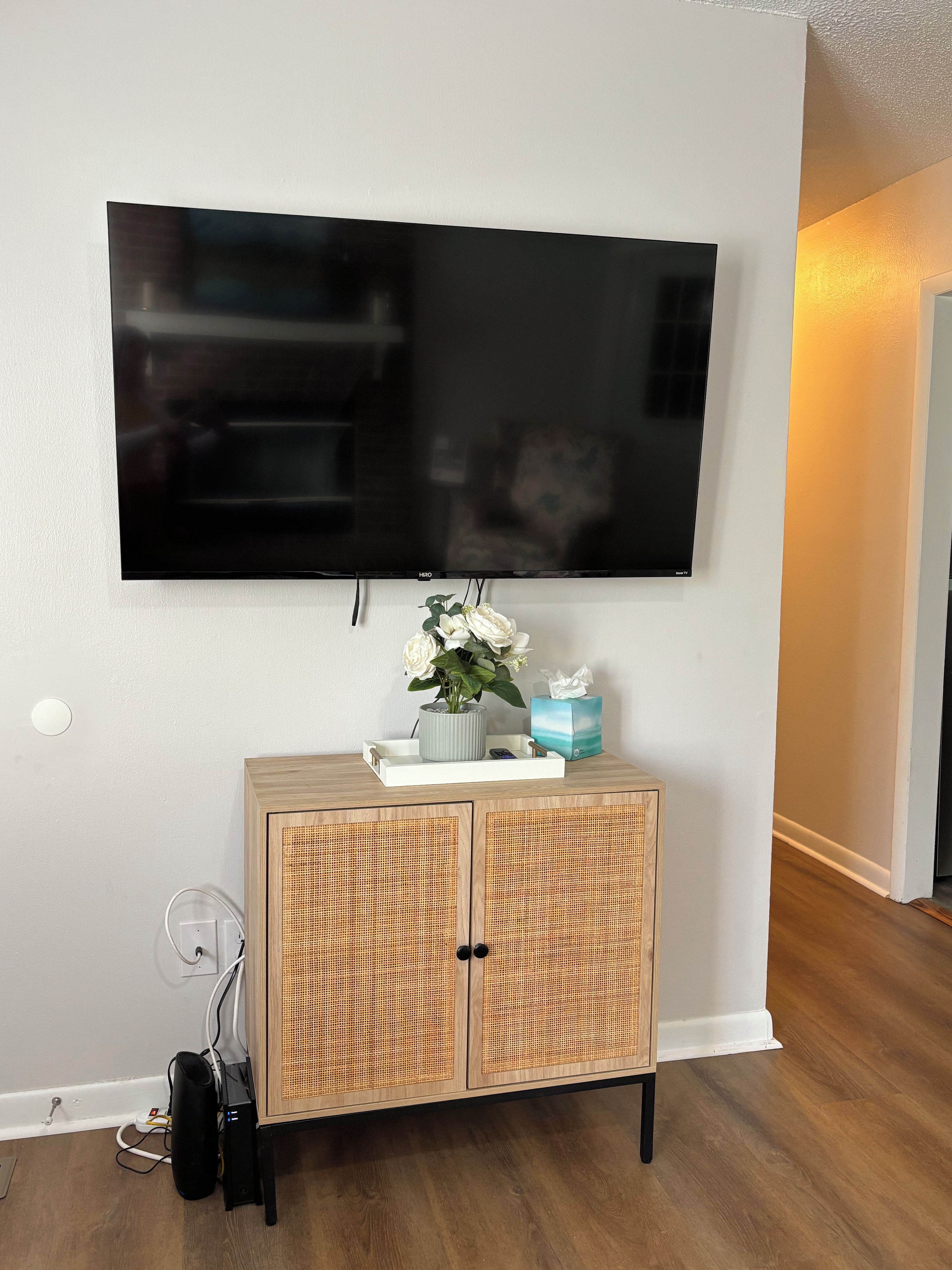 Un televisor de pantalla plana montado en una pared, sobre un mueble de madera con puertas de mimbre.
