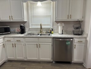 Una cocina con armarios blancos, lavavajillas de acero inoxidable, microondas y un lavabo con grifo.