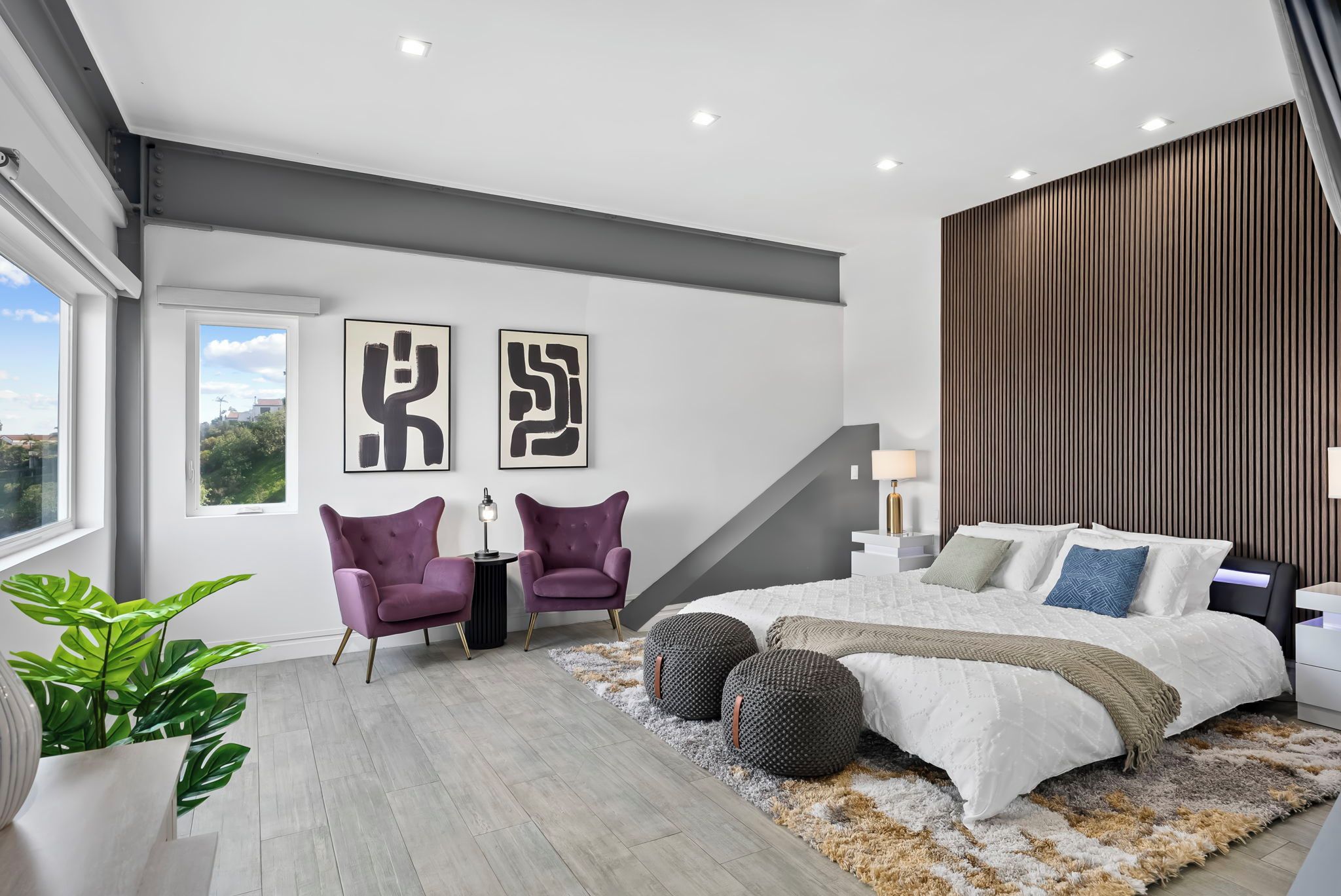 A modern bedroom with a large bed, two armchairs, a small table, and abstract art on the wall.