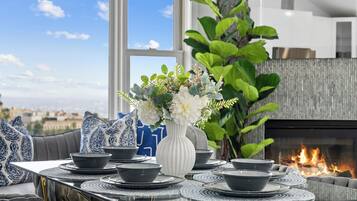 A dining area with a table set for four, a white vase with flowers, and a fire feature in the background.