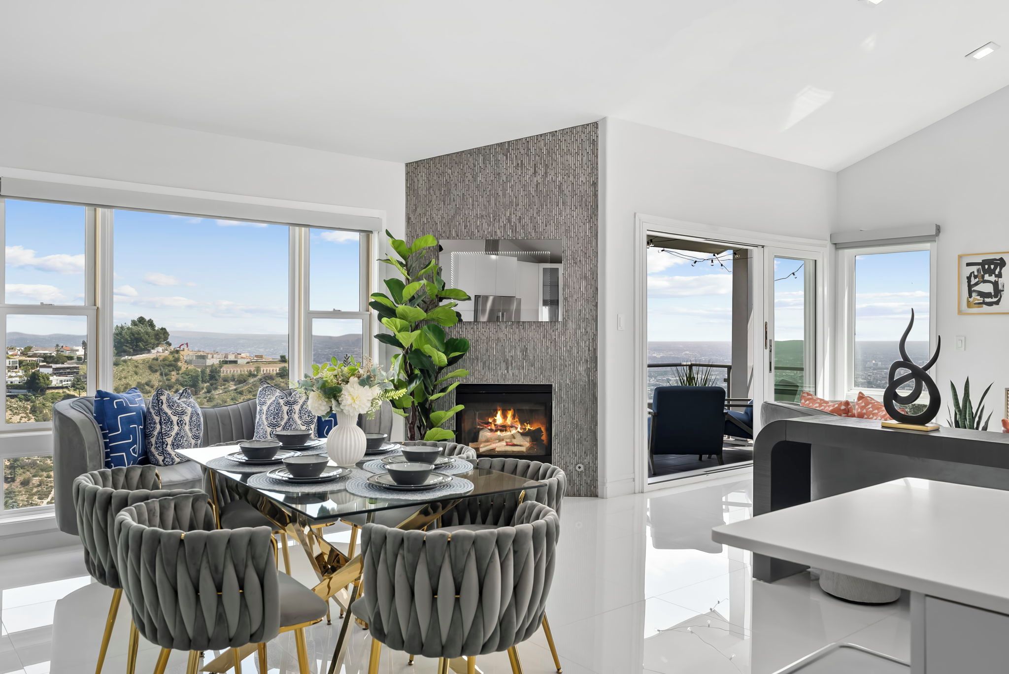 A modern living room with a fireplace, a dining area with a glass table, and large windows offering a city view.