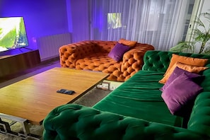Una sala de estar con un sofá verde, un sillón naranja con capitonado y una mesa de centro de madera.