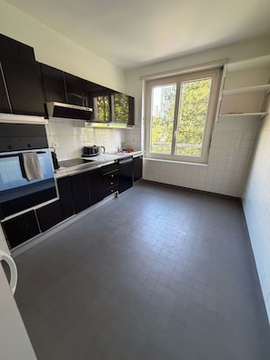 A modern kitchen with black cabinets, a stainless steel range, and a window providing a view of greenery outside. - Spacious 2-Bedroom Apartment in Central Lausanne (Lausanne)