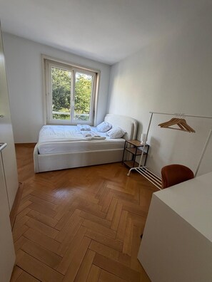 Ein Schlafzimmer mit einem Bett, einem Fenster, einem Holzboden, einem weißen Schreibtisch und einem roten Stuhl.