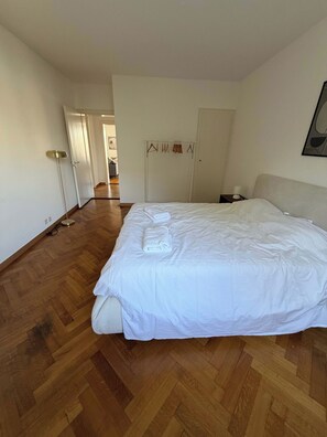 Een slaapkamer met een groot bed, een kledingkast, een nachtkastje en een vloerlamp.