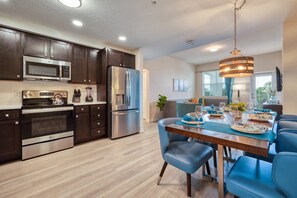 A modern kitchen with dark wood cabinets, stainless steel appliances, and a dining area with blue chairs and a wooden table set for a meal. - Vista Cay 3BR Condo King Suite Near Universal (Orlando)