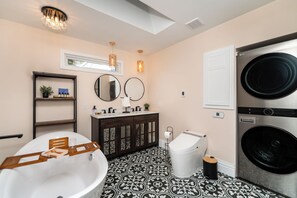 Un baño moderno con una bañera independiente, un inodoro, un lavamanos con espejo y una lavadora.