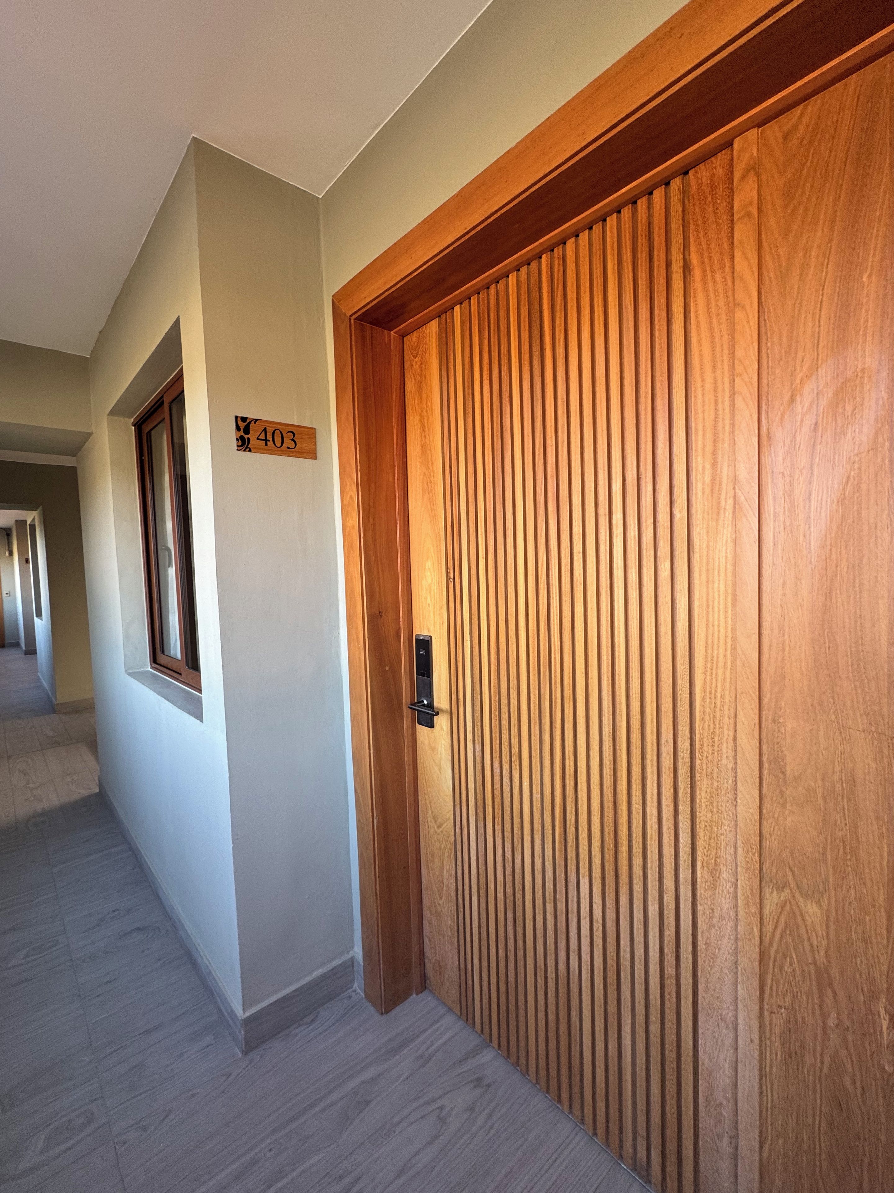 Un pasillo con una puerta de madera, un cartel con un número y una ventana.