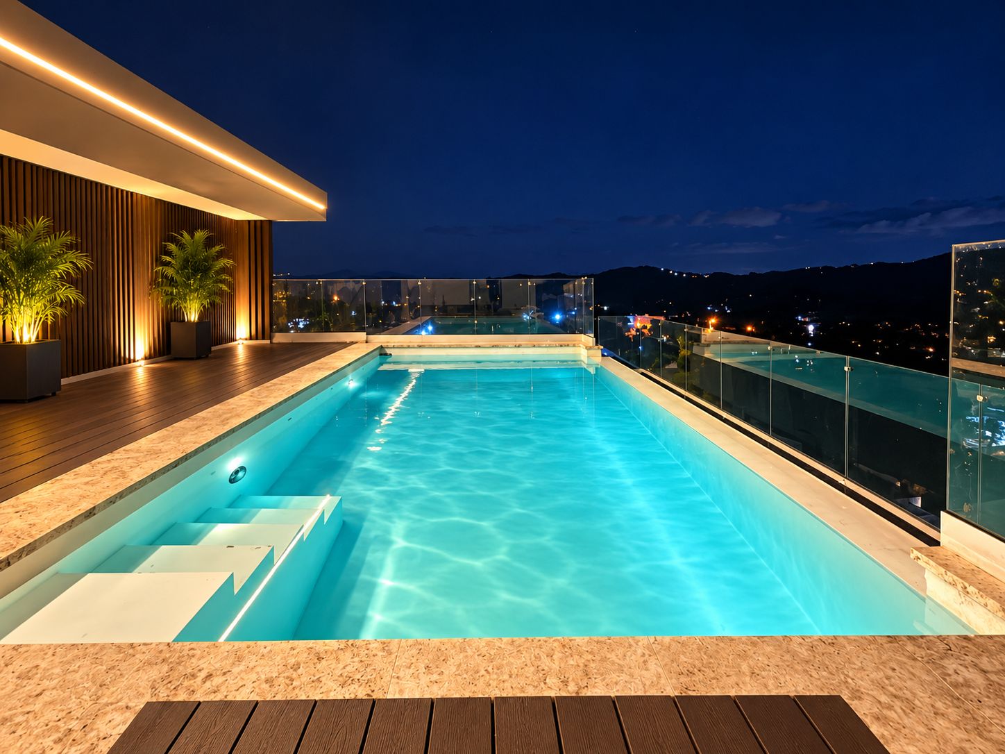 Una piscina infinita en la azotea con cubierta de madera y barandilla de vidrio, con vistas a un paisaje urbano nocturno.