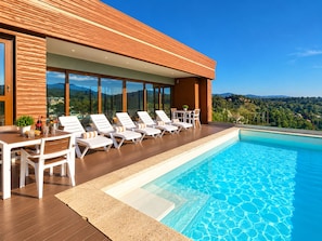 A modern outdoor pool area with lounge chairs and a table, surrounded by wooden deck and glass windows. - New Listing (Jarabacoa)