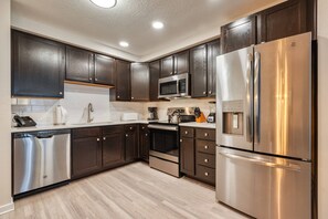 A modern kitchen with dark wood cabinets, stainless steel appliances, and a light wood floor. - Vista Cay 3BR Condo King Suite Near Universal (Orlando)
