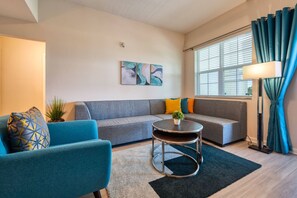 A modern living room with a grey sofa, a blue armchair, a round coffee table, and a floor lamp. - Vista Cay 3BR Condo King Suite Near Universal (Orlando)