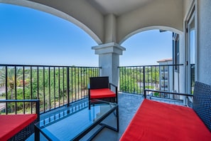 Ein Balkon mit einem Glastisch, zwei Stühlen mit roten Kissen und Blick auf Grünflächen und Gebäude.