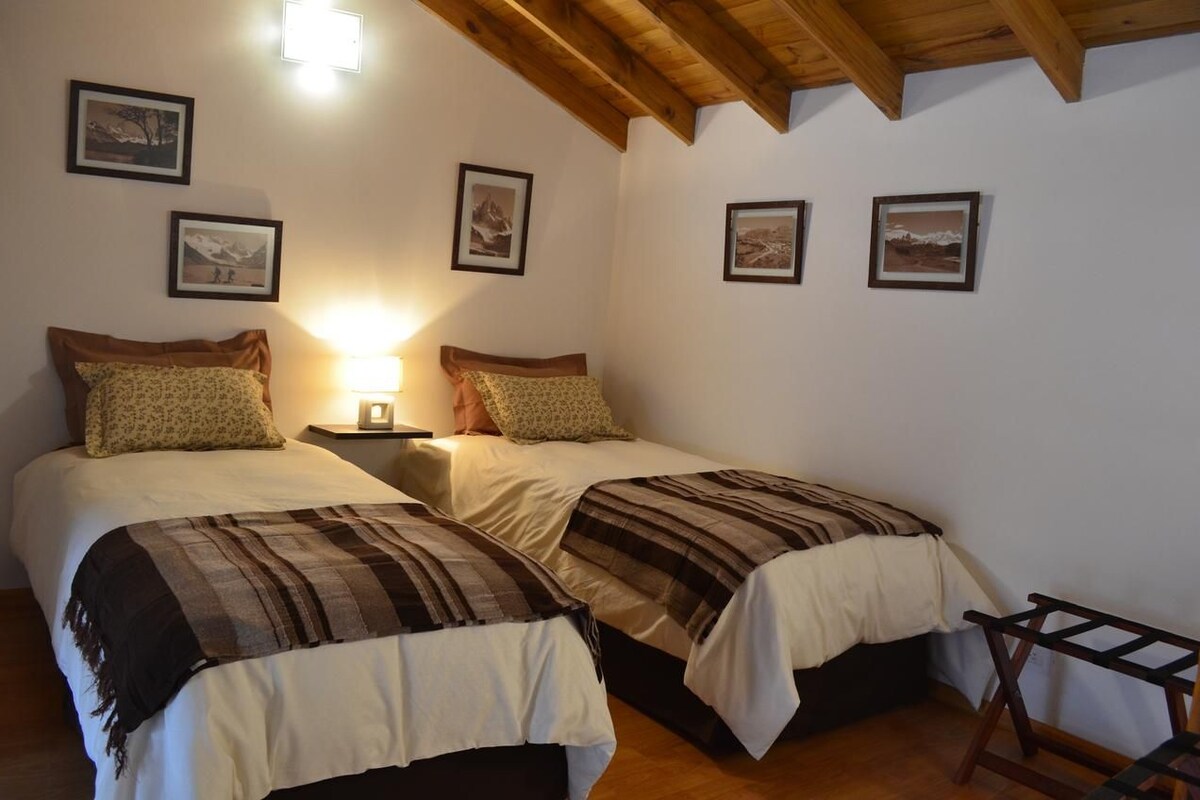 Un dormitorio con dos camas, una mesita de noche, una lámpara y cuadros enmarcados en la pared.