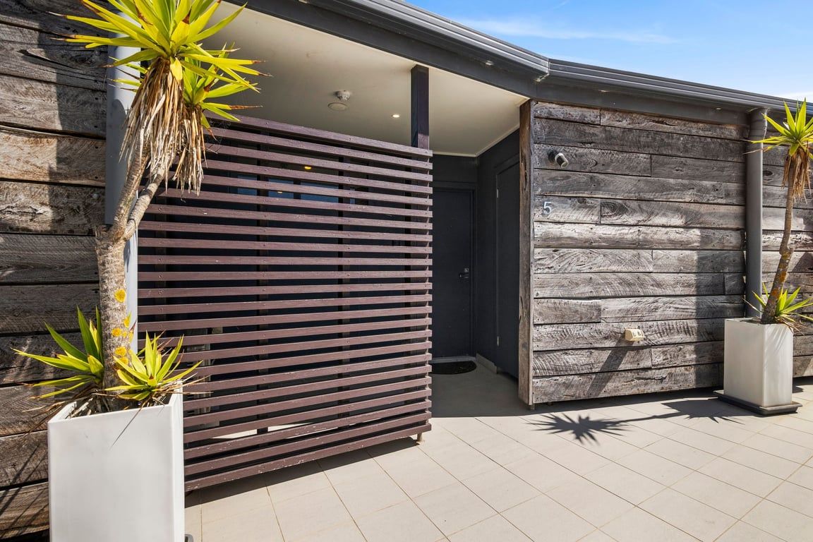 A modern building with a wooden facade, a sliding door, and potted plants.