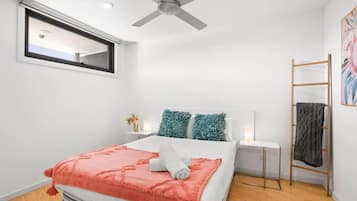 A bedroom with a bed, a ceiling fan, a window, a bedside table with a lamp, and a wooden ladder.