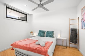 Ein Schlafzimmer mit einem Bett, einem Deckenventilator, einem Fenster, einem Nachttisch mit Lampe und einer Holzleiter.