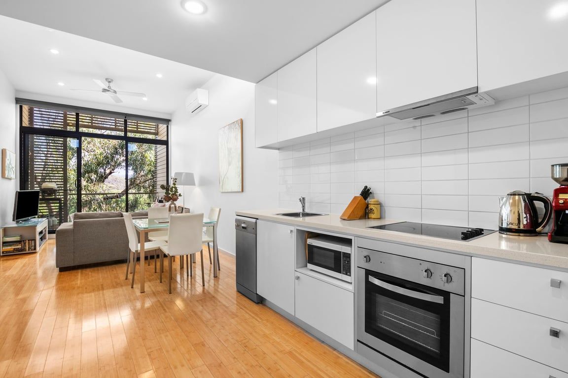 Una cocina moderna con armarios blancos, horno integrado y un comedor con sofá y mesa.