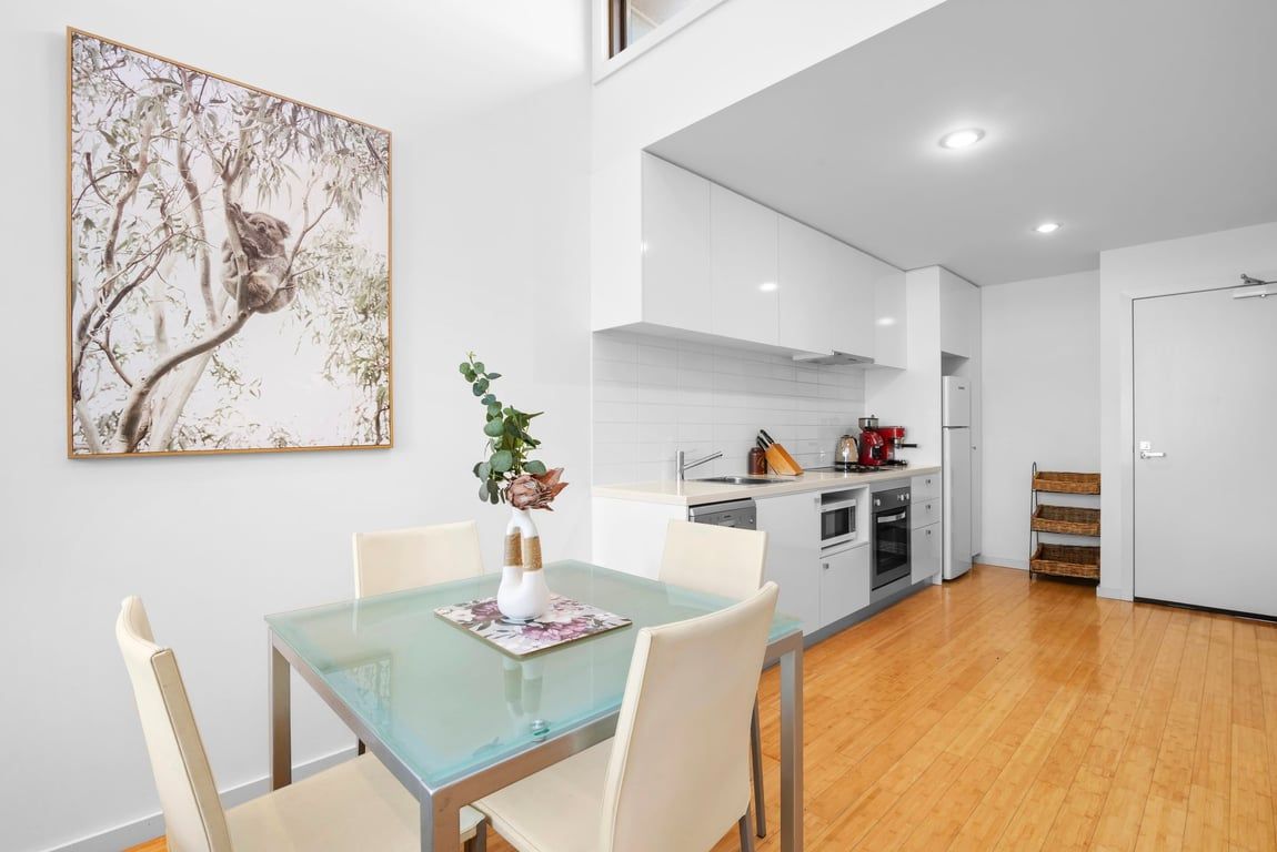 Una cocina moderna con armarios blancos, una mesa de comedor de vidrio y un cuadro con un árbol.