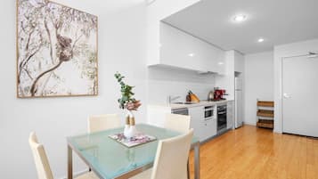 Una cocina moderna con armarios blancos, una mesa de comedor de vidrio y un cuadro con un árbol.