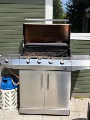 A stainless steel outdoor grill with four burners, a side cabinet, and a blue propane tank. - Beautiful cottage close to forest and beach (Væggerløse)