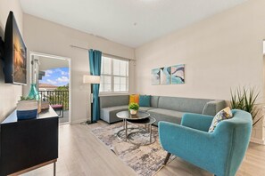 A modern living room with a grey sofa, teal armchairs, a coffee table, and a TV mounted on the wall. - Vista Cay 3BR Condo King Suite Near Universal (Orlando)