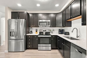 A modern kitchen with stainless steel appliances, dark cabinetry, and a white countertop. - Vista Cay 3BR Condo King Suite Near Universal (Orlando)
