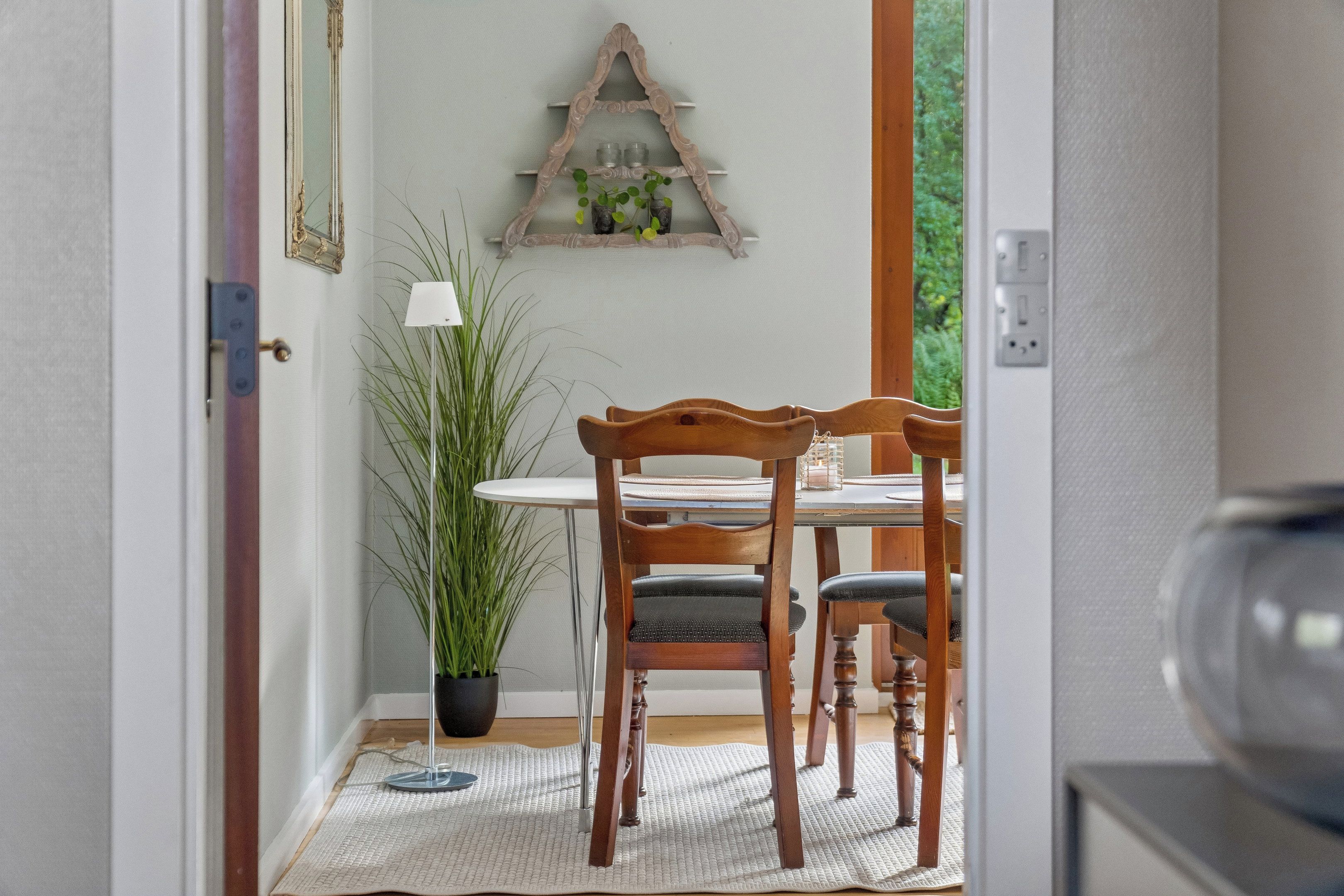 A dining area with a table and chairs, a potted plant, and a wall-mounted shelf with candles.