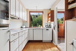 A compact kitchen with white cabinets, a built-in dishwasher, and a window with a view of greenery. - Holiday home near lake, nature and coast (Faldsled)