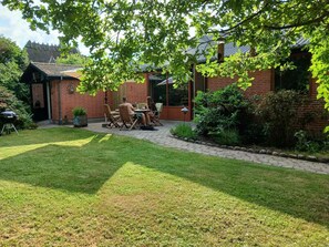 A brick house with a patio, a barbecue grill, and a dining area with chairs and a table. - Holiday home near lake, nature and coast (Faldsled)