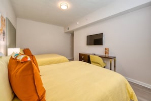 Ein Hotelzimmer mit zwei Betten, einem Schreibtisch, einem Stuhl, einem Flachbildfernseher und einer Deckenleuchte.