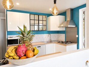 A modern kitchen with white cabinets, a stainless steel range hood, and a bowl of fruit on the counter. - New Listing (Le Diamant)