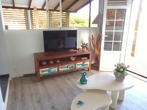 A room with a television on a wooden cabinet, a small white table with a vase, and a door with glass panels. - New Listing (Le Diamant)