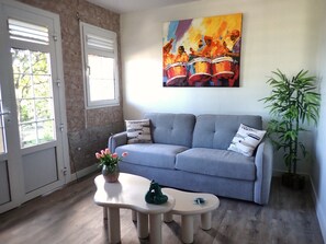 A living room with a grey sofa, two side tables, a painting, a window, and a bamboo plant. - New Listing (Le Diamant)