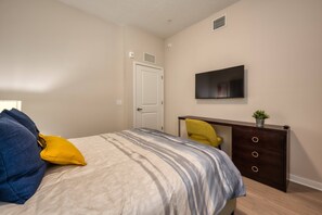 A bedroom with a bed, a desk, a chair, a television, and a door. - Vista Cay 3BR Condo King Suite Near Universal (Orlando)