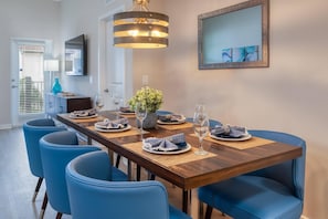 A dining area with a wooden table set for four, blue chairs, and a hanging light fixture. - Vista Cay 3BR Condo King Suite Near Universal (Orlando)