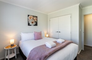 A hotel room with a bed, bedside lamps, a wardrobe, and a painting on the wall. - Kopakopa Rest - Taupo (Taupo)